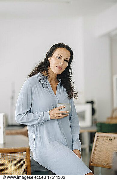 Female owner holding coffee mug while sitting on table in restaurant