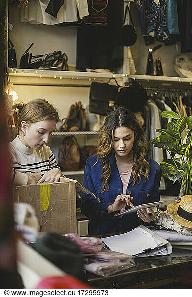 Female owner making note on digital tablet standing by colleague in clothing store