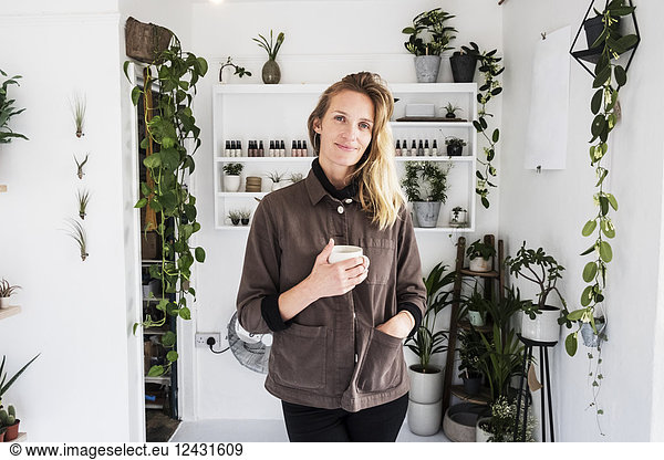 Female owner of plant shop smiling at camera  a selection of plants on wooden shelves.