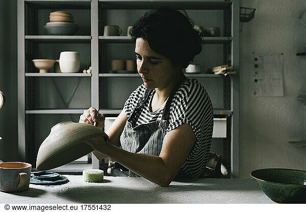 Female owner painting bowl at table in ceramics store