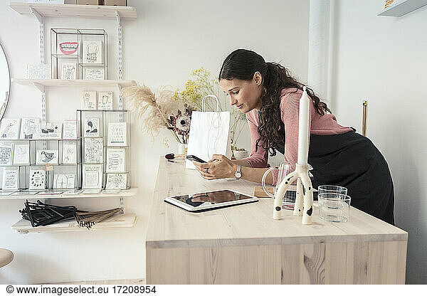 Female owner using smart phone while leaning on table in design studio