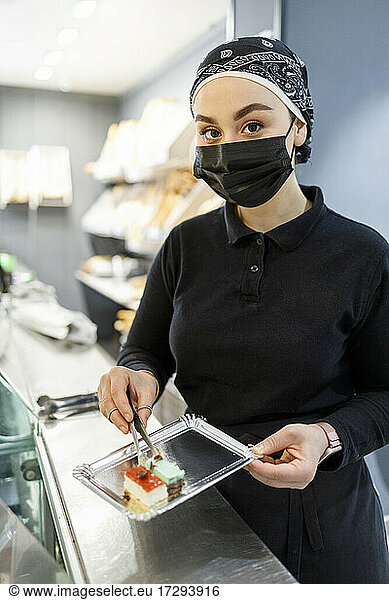 Female owner wearing bandana holding tray with cake at bakery