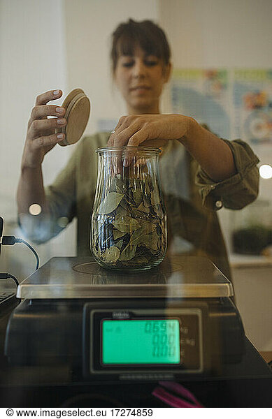 Female owner weighing leaf jar on weight scale in cafe