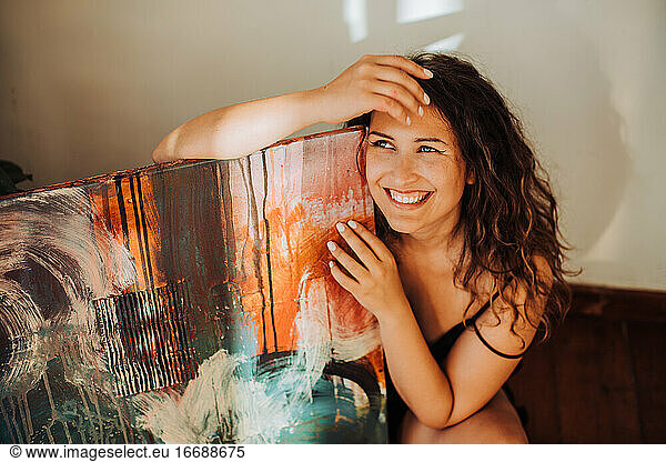 Female painter holding her abstract art on canvas and smiling