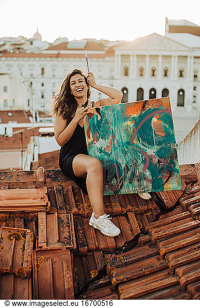 Female painter sitting on rooftop with abstract art painting and brush