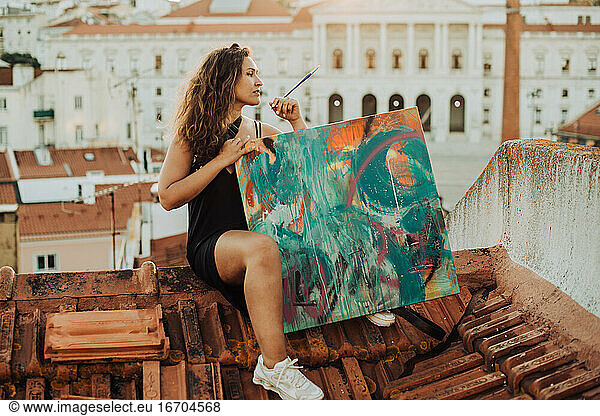 Female painter with abstract art canvas sitting on the roof in Lisbon