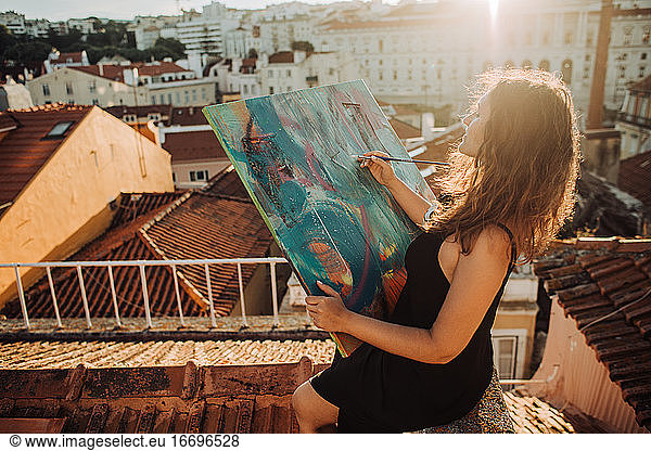 Female painter with abstract art canvas working on the roof
