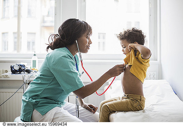 Female pediatrician examining boy's heartbeat in medical clinic