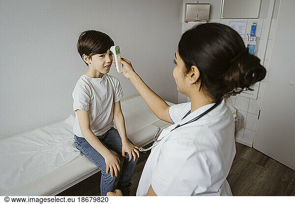 Female pediatrician measuring temperature of boy through infrared thermometer at hospital
