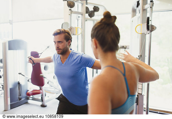 Female personal trainer guiding man doing cable chest fly at gym