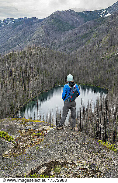 Female poses above an alpine lake surrounded by burned dead trees