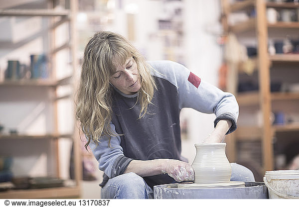 Female potter forming clay pot on pottery wheel in workshop