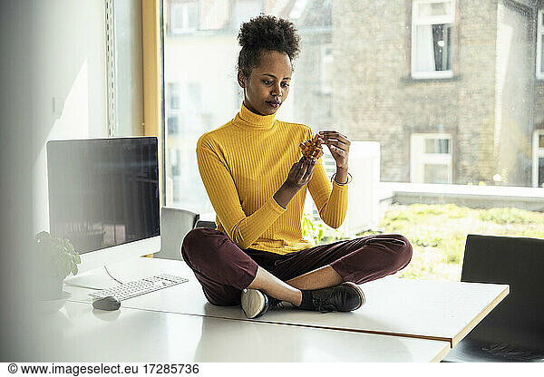 Female professional assembling wooden cube puzzle while sitting on desk in office
