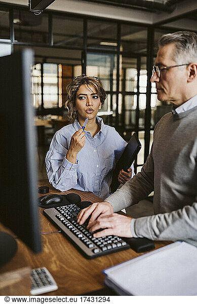 Female professional discussing with businessman using computer at desk