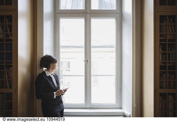 Female professional listening music while looking through window at library