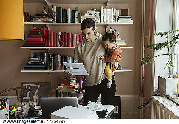 Female professional reading document while carrying son at home office
