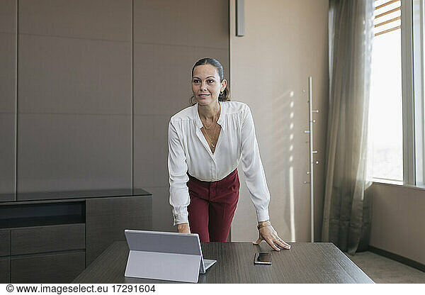 Female professional with laptop and mobile phone standing at desk in office