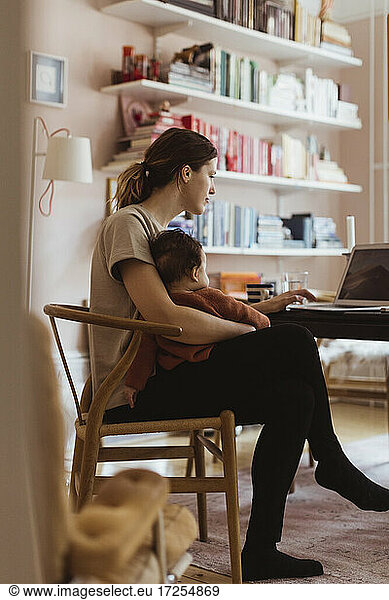 Female professional working on laptop while sitting with baby boy at home office