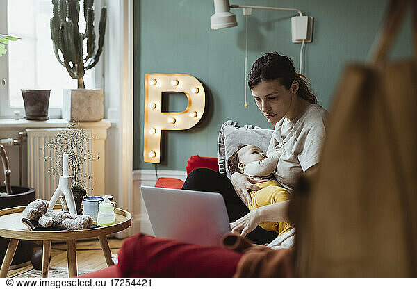 Female professional working on laptop while taking care of baby boy at home