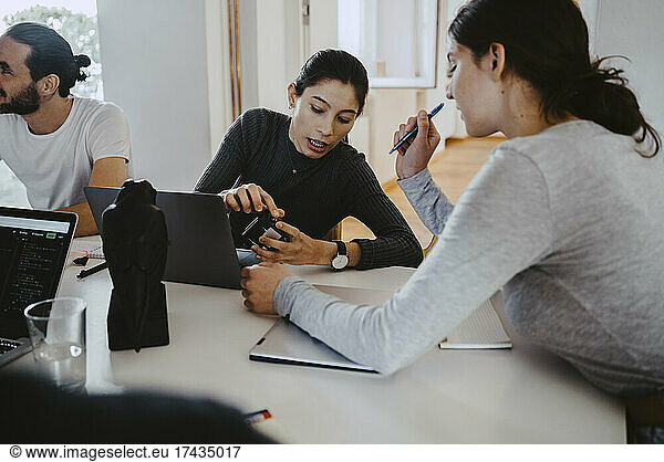 Female professionals discussing over satellite finder at table in creative office