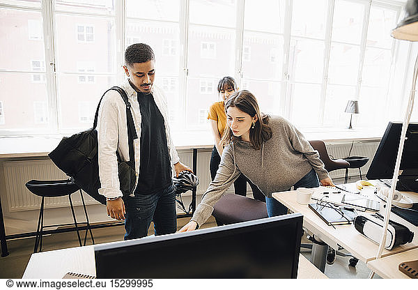 Female programmer showing computer to coworkers against window in office