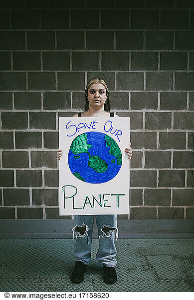Female protestor with planet earth poster standing on footpath against wall