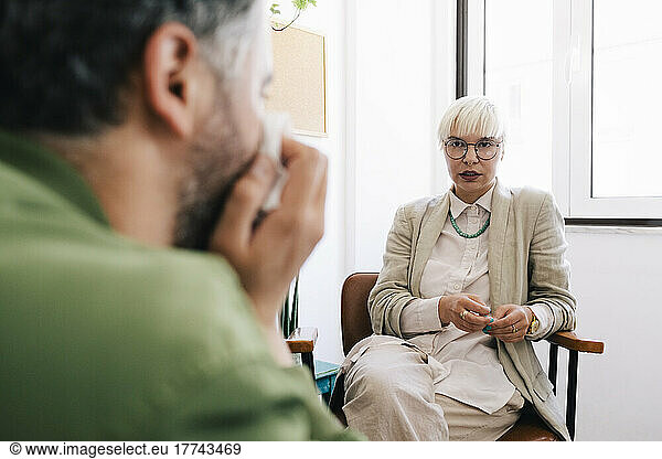 Female psychotherapist discussing with male patient sitting at therapy office