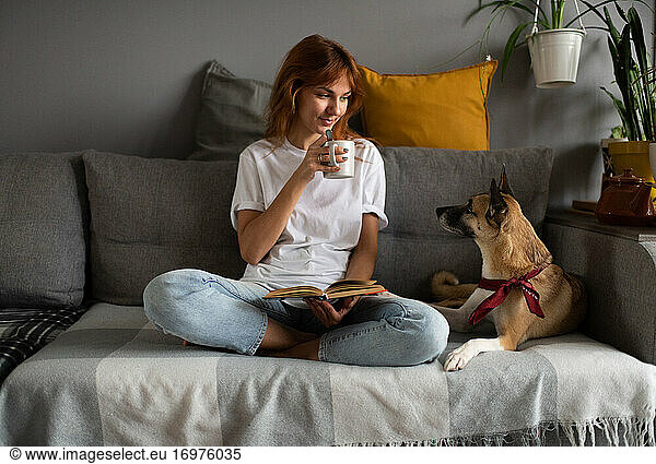 Female reader drinking hot beverage near dog