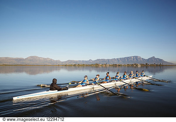 Female rowers rowing scull on sunny lake under blue sky