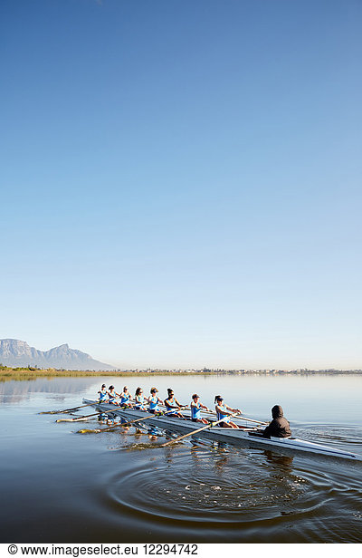 Female rowers rowing scull on tranquil lake under blue sky