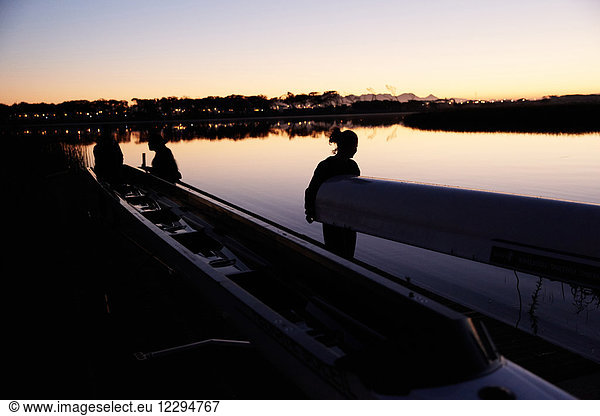 Female rowing team carrying scull at sunrise lake