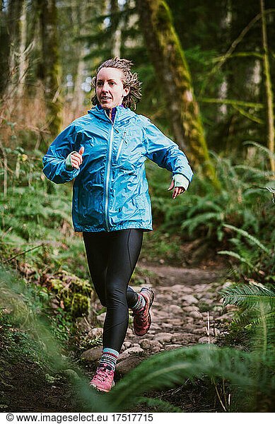Female runner in blue jacket on rocky trail surrounded by ferns