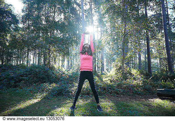 Female runner stretching arms and warming up in sunlit forest