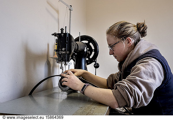 Female saddler sitting in workshop  sewing on saddlery sewing machine.