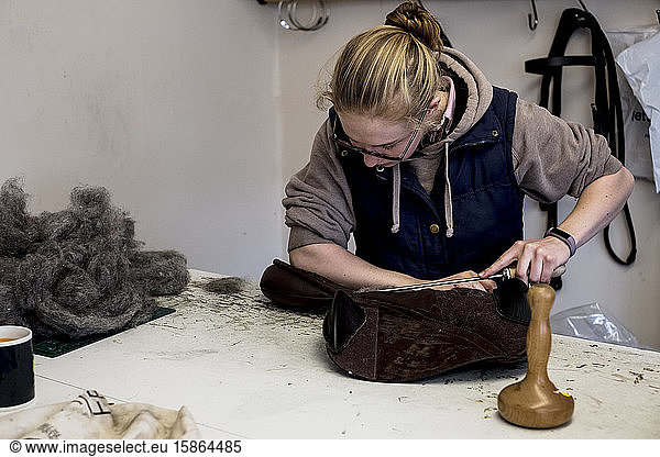 Female saddler standing in workshop  stuffing leather saddle with horse hair.