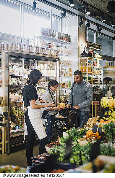 Female sales clerk talking with customers buying groceries at delicatessen