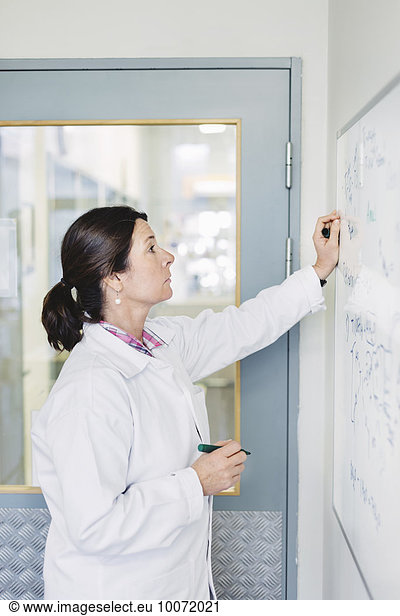 Female scientist analyzing plan on whiteboard at laboratory