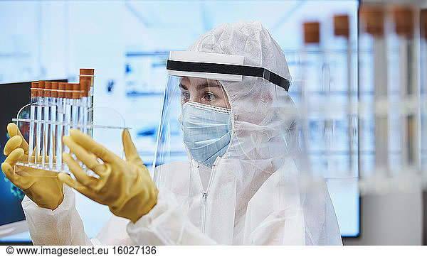 Female scientist in clean suit with test tubes studying coronavirus