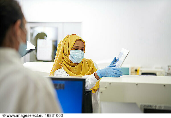 Female scientist in hijab and face mask using digital tablet