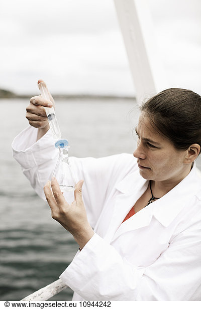 Female scientist injecting water in flask on boat in sea