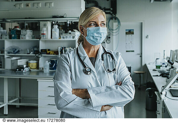 Female scientist wearing face mask standing with arms crossed at laboratory