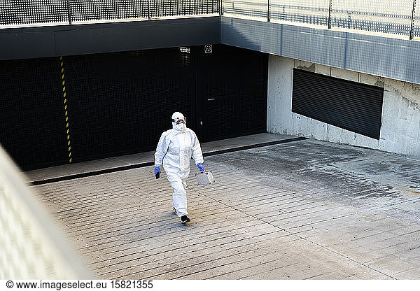 Female scientist wearing protective suit and mask and walking at a garage