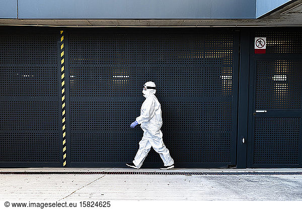 Female scientist wearing protective suit and mask and walking in front of a wall