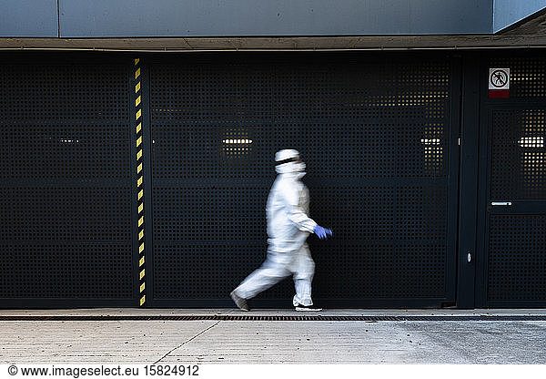 Female scientist wearing protective suit and mask and walking in front of a wall