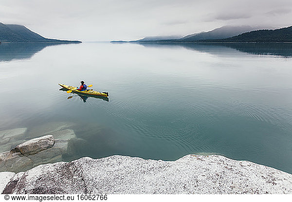 Female sea kayaker paddling pristine waters of Muir Inlet overcast sky in distance Glacier Bay National Park Alaska
