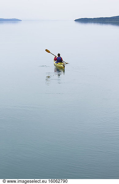 Female sea kayaker paddling pristine waters of Muir Inlet overcast sky in distance Glacier Bay National Park Alaska