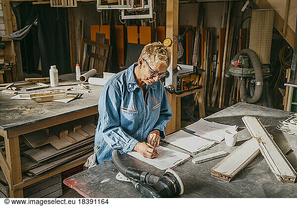 Female senior entrepreneur preparing document over workbench at repair shop