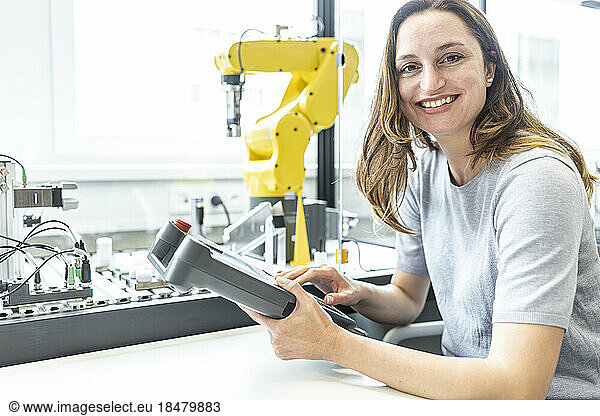 Female skilled worker in robotic factory controlling robot arm with digital control