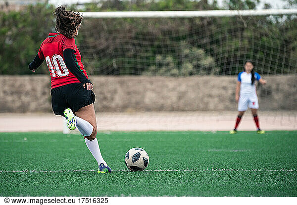Female soccer player kicks the ball towards the goal in a stadium