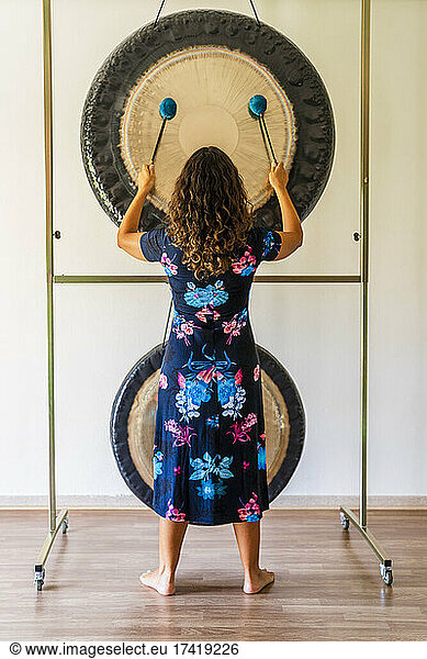 Female sound therapist playing gong while standing in studio